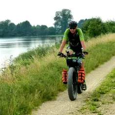 Rowerzysta w kasku i sportowym stroju przemierza piaszczystą ścieżkę nad jeziorem, ciesząc się turystyką rowerową.
