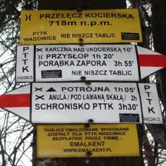 Znaki szlaku PTTK na drzewie wskazują drogę na Przełęcz Kocierską, do schroniska i innych punktów.