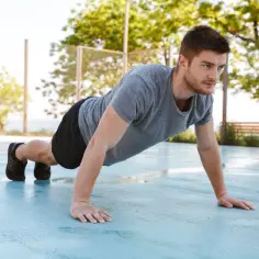 Mężczyzna wykonuje pompki na świeżym powietrzu, wzmacniając mięśnie, w tym pompki na biceps.