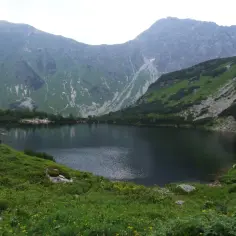Górskie jezioro cyrkowe otoczone zielonymi zboczami i skalistymi szczytami.