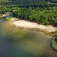 Malownicze pogoria jezioro z piaszczystą plażą, lasem i budynkiem ośrodka wypoczynkowego.