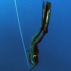 Nurkini w czarnym skafandrze, z płetwami na nogach, opada w głąb oceanu, kierując się liną. To moment bicia freediving rekord.