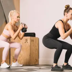 Dwie kobiety wykonują przysiady z kettlebellami. To świetny trening cardio i siłowy.