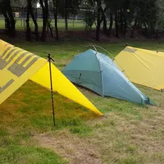Żółty tarpa z napisem "OUTDOOR" i zielony namiot na trawie.