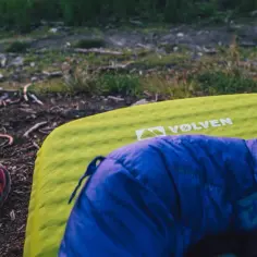 Czerwone buty Salomon i niebieski śpiwór leżą na zielonej kalimacie obok namiotu.