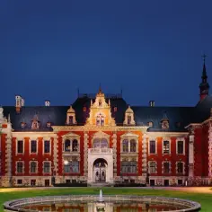 Pałac w Pławniowicach nocą, z fontanną na pierwszym planie. Architektura pałacu zachwyca, to jedna z głównych atrakcji regionu.