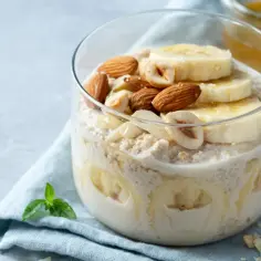 Nocna owsianka z bananem, migdałami i orzechami w szklance, polana miodem.