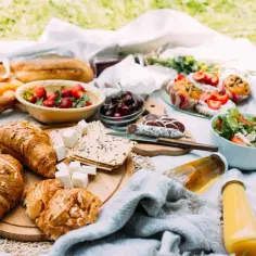 Pyszne jedzenie na piknik: świeże croissanty, bagietka, owoce, sałatka, kiełbasa i napoje. Idealny zestaw na słoneczny dzień.