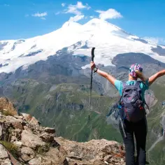 Turystka z plecakiem i kijkami trekkingowymi podziwia najwyższy szczyt Rosji, Elbrus, pokryty śniegiem.