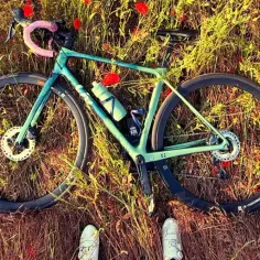 Zielony rower leży wśród maków. Widać ustawienie siodełka w rowerze, butelkę na wodę i fragmenty kół.