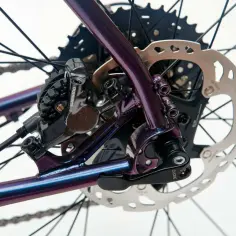 Błyszcząca, fioletowa rama roweru z widoczną sztywną osią, hamulcem tarczowym Shimano i kasetą.