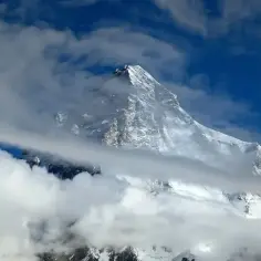 Śnieżny szczyt K2, najwyższy szczyt Karakorum, przebija się przez chmury na tle błękitnego nieba.