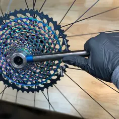 Rękawiczka mechanika dokręca śrubę w kolorowym wolnobiegu rowerowym SRAM Eagle.
