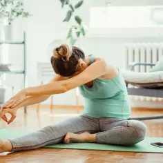 Kobieta wykonuje ćwiczenia **stretching co to** jest, siedząc na macie w domu.