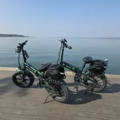 Dwa zielone rowery elektryczne z sakwami, gotowe na wyprawę z zasięgiem 200 km nad spokojną wodą.