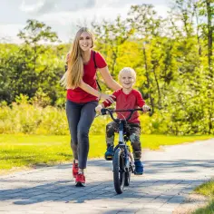 Mama uczy synka, jak nauczyć dziecko jeździć na rowerze. Radosny chłopiec pedałuje, a mama go asekuruje.