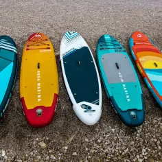 Pięć desek SUP, w tym modele Aqua Marina i Gladiator, leży na plaży. Ranking desek sup może pomóc w wyborze idealnej.