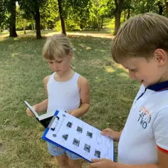 Dzieci rozwiązują ciekawe zadania na podchody w parku, identyfikując drzewa na podstawie zdjęć.