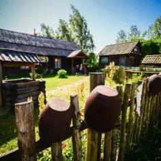 Skansen na wyżynie krakowsko-częstochowskiej: drewniane chaty, studnia i gliniane garnki na płocie.