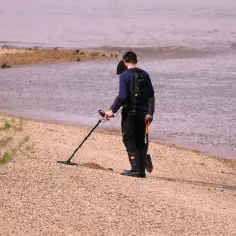 Mężczyzna z wykrywaczem metali i łopatką na plaży.