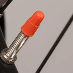 Pomarańczowa nakrętka na wentyl rowerowy, jeden z rodzajów wentyli rowerowych.