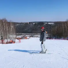 Narciarz w kasku i goglach na stoku narciarskim, w tle drzewa i zabudowania.
