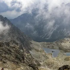 Kamienisty szlak na Rysy wije się wśród skalistych zboczy i mgieł. W dole widać dwa górskie stawy.