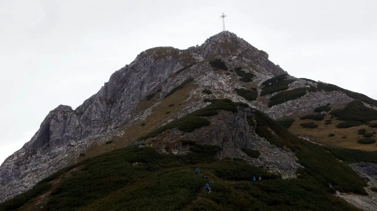 Turyści wspinają się na Giewont, podziwiając skaliste zbocza i zielone kosodrzewiny. Widać, ile się wchodzi na Giewont, gdy szlak pnie się ku górze.