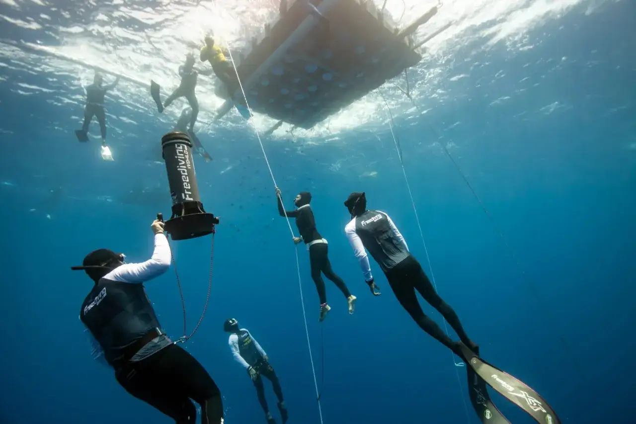 Pod wodą, freediverzy przygotowują się do bicia freediving rekord. Widać platformę, liny i sprzęt do pomiaru głębokości.