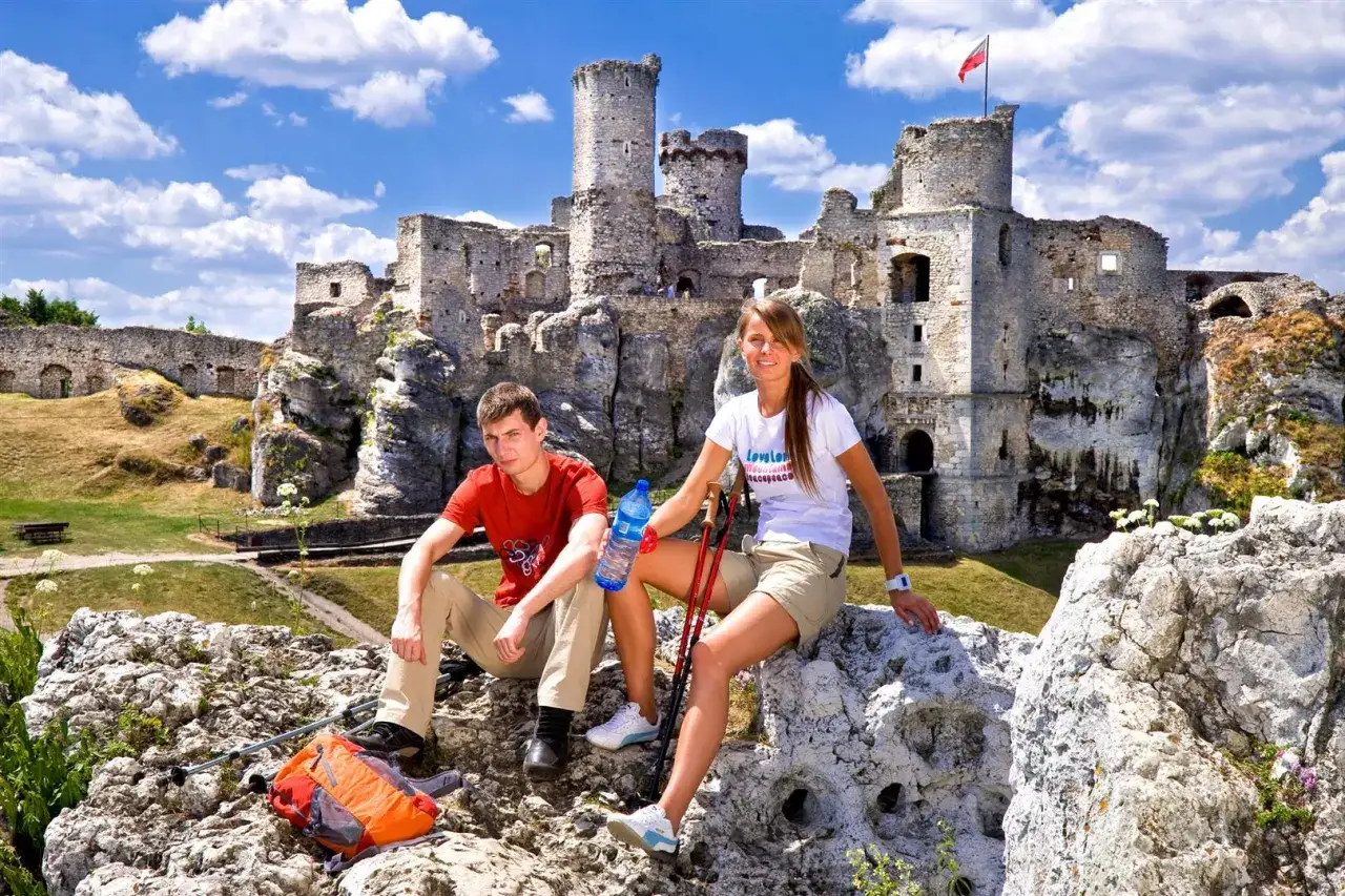 Para zwiedza ruiny zamku Ogrodzieniec, siedząc na skale z kijkami trekkingowymi.