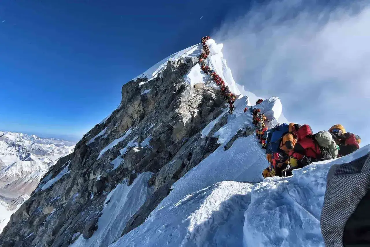 Kolejka szerpów i alpinistów na zboczu góry, wspinających się w trudnych warunkach.