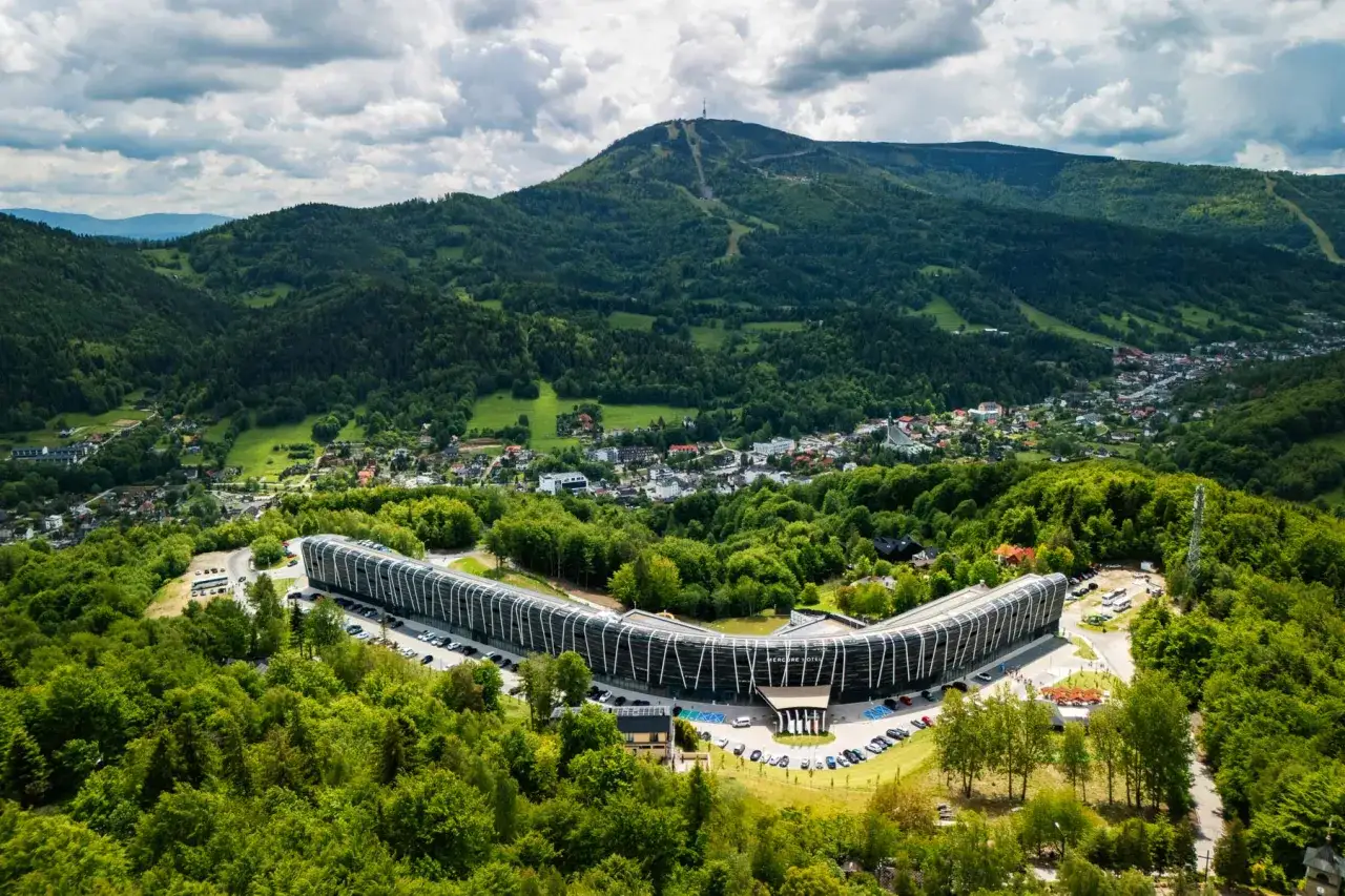 Nowoczesny hotel Orle Gniazdo Szczyrk w otoczeniu zielonych gór, z widokiem na miasteczko i szczyt Skrzyczne.