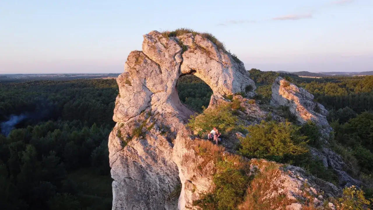 Para zakochanych na skale z otworem, na tle lasów i pól na Wyżynie Krakowsko-Częstochowskiej.
