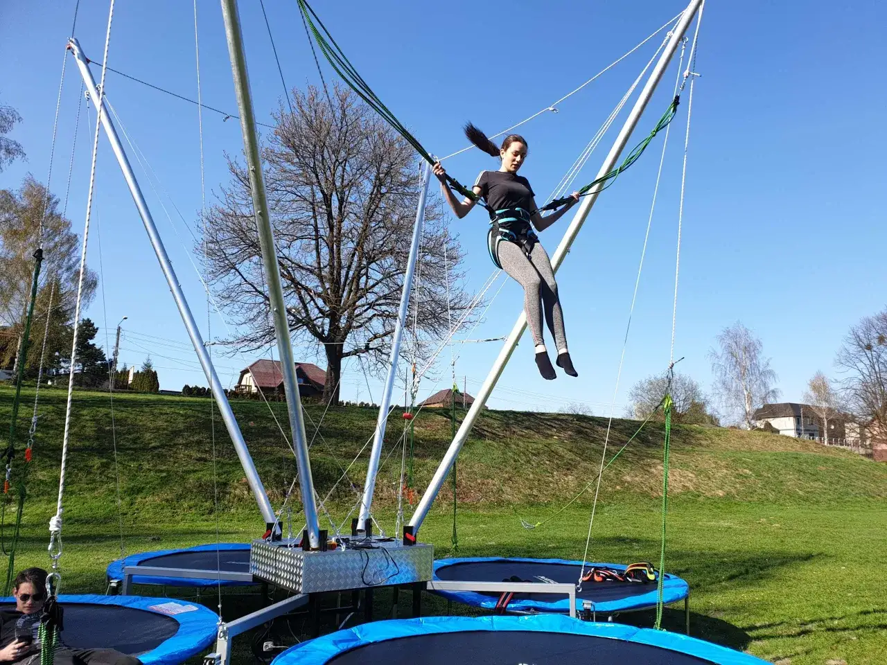 Dziewczyna w uprzęży skacze na eurobungee, unosząc się wysoko nad trampolinami.