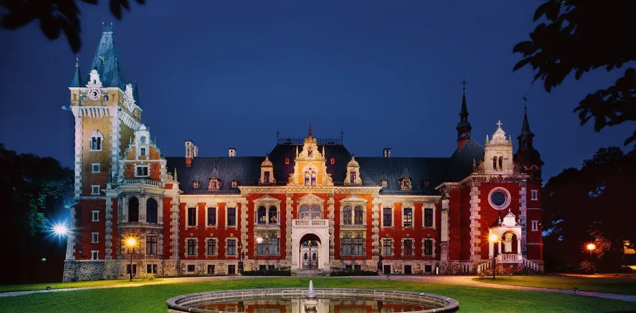 Pałac w Pławniowicach nocą, z fontanną na pierwszym planie. Architektura pałacu zachwyca, to jedna z głównych atrakcji regionu.