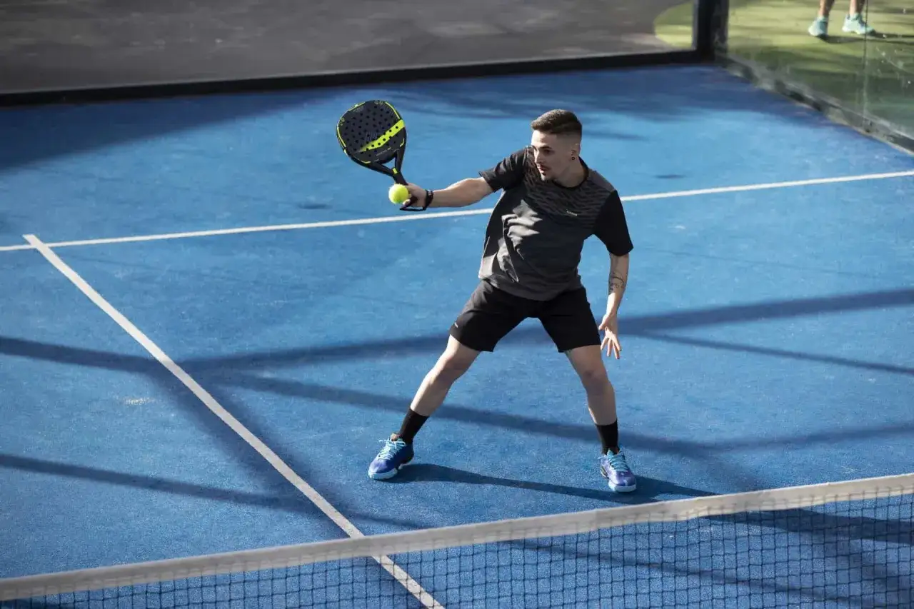 Mężczyzna gra w padel, sport, który łączy tenis i squasha. Widok na niebieski kort z siatką.