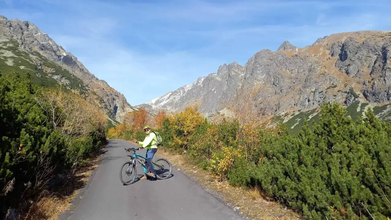 Rowerzysta na tle gór, gdzie znajduje się najwyższy szczyt Karpat. Jesienne barwy drzew i skaliste zbocza.