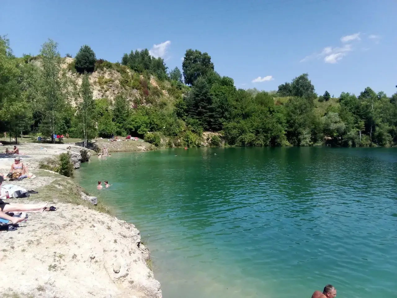 Turkusowa woda i skaliste zbocza tworzą malowniczy polski Balaton. Ludzie odpoczywają na brzegu i kąpią się w krystalicznie czystej wodzie.