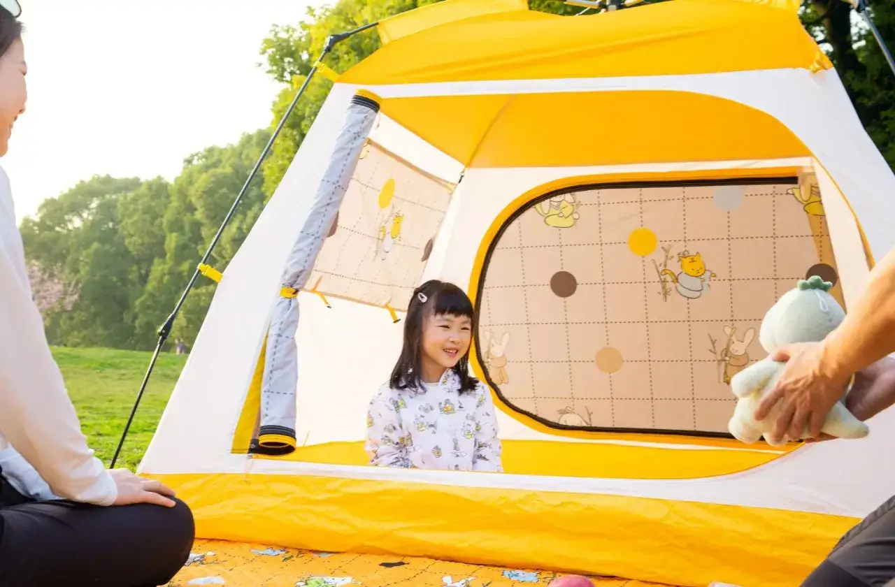 Rodzina cieszy się wspólnym składaniem namiotu plażowego. Uśmiechnięta dziewczynka w środku, rodzice na zewnątrz.