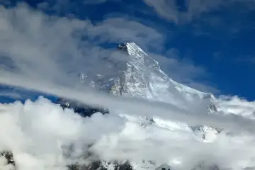 Śnieżny szczyt K2, najwyższy szczyt Karakorum, przebija się przez chmury na tle błękitnego nieba.