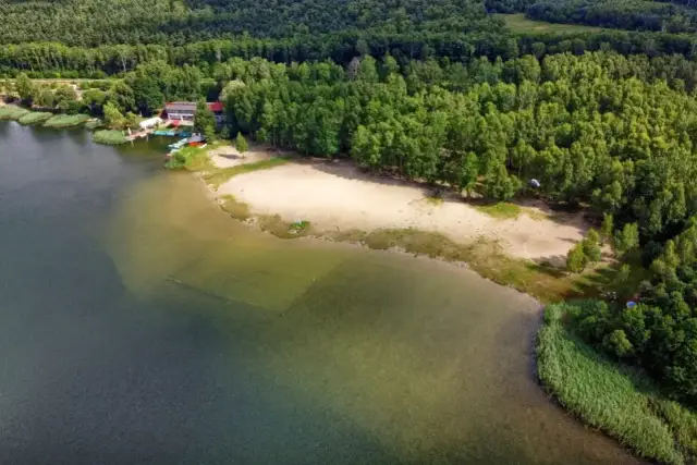 Malownicze pogoria jezioro z piaszczystą plażą, lasem i budynkiem ośrodka wypoczynkowego.